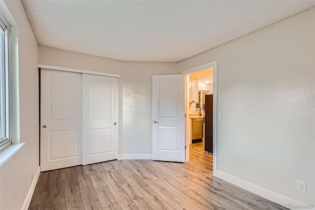 unfurnished bedroom with light wood-style floors, a textured ceiling, baseboards, and a closet