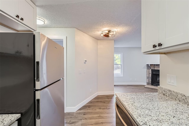 kitchen featuring light wood finished floors, white cabinets, appliances with stainless steel finishes, a textured ceiling, and a fireplace