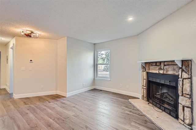 unfurnished living room with a fireplace, a textured ceiling, baseboards, and wood finished floors