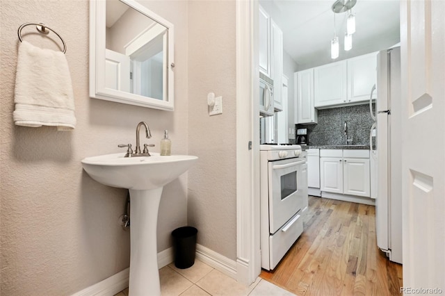 kitchen featuring white appliances, sink, light hardwood / wood-style flooring, decorative backsplash, and white cabinetry