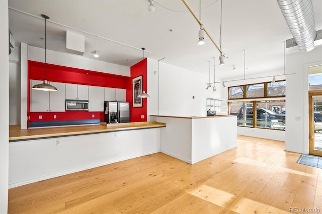 kitchen with light wood-type flooring, stainless steel appliances, hanging light fixtures, and kitchen peninsula