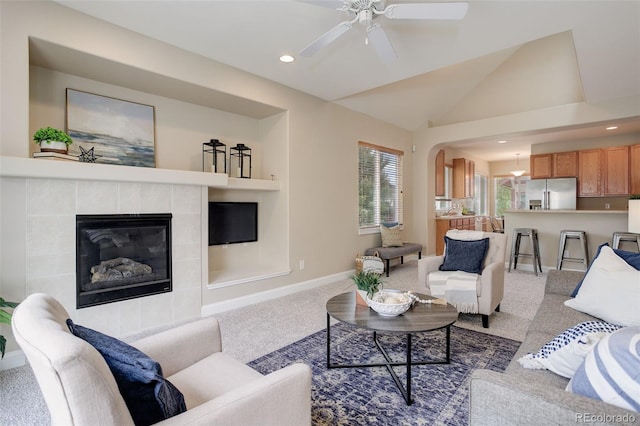 living room with a tile fireplace, vaulted ceiling, carpet floors, ceiling fan, and built in shelves