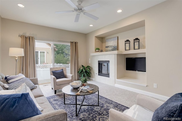 carpeted living room featuring a tiled fireplace, built in shelves, and ceiling fan