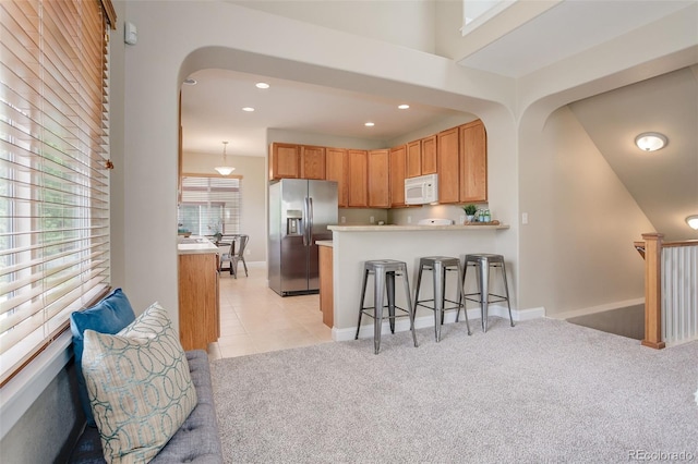 kitchen featuring light carpet, a breakfast bar area, stainless steel fridge with ice dispenser, and hanging light fixtures