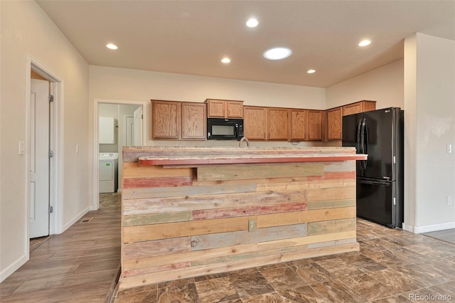 kitchen with a kitchen breakfast bar, washer / clothes dryer, a center island with sink, and black appliances