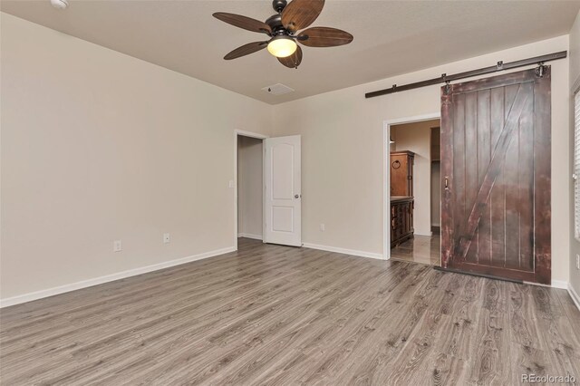 unfurnished bedroom featuring a barn door, light hardwood / wood-style flooring, ensuite bath, and ceiling fan