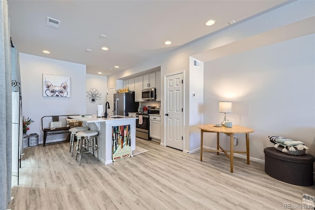 kitchen featuring sink, light hardwood / wood-style flooring, an island with sink, a kitchen bar, and appliances with stainless steel finishes