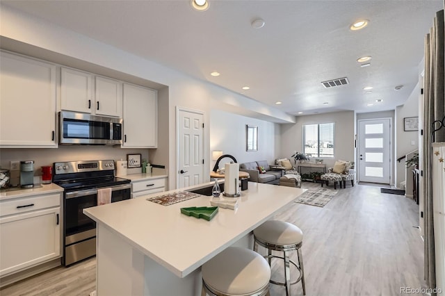 kitchen featuring white cabinets, appliances with stainless steel finishes, a kitchen island with sink, and a kitchen breakfast bar