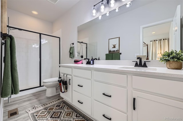 bathroom featuring toilet, vanity, a shower with shower door, and hardwood / wood-style flooring