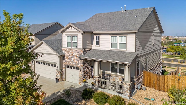 craftsman-style house with driveway, a shingled roof, stone siding, fence, and a porch