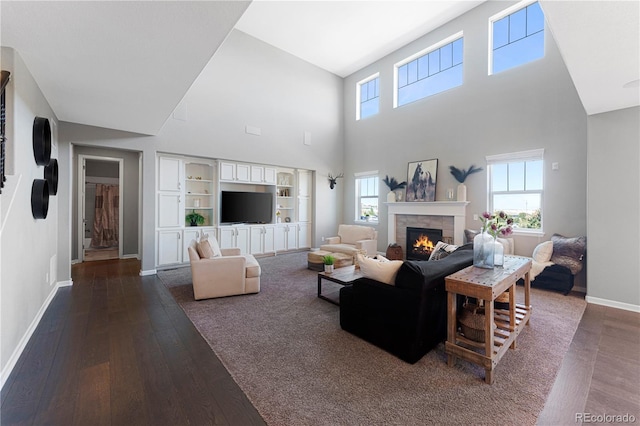 living room with dark wood-style flooring, plenty of natural light, a lit fireplace, and baseboards