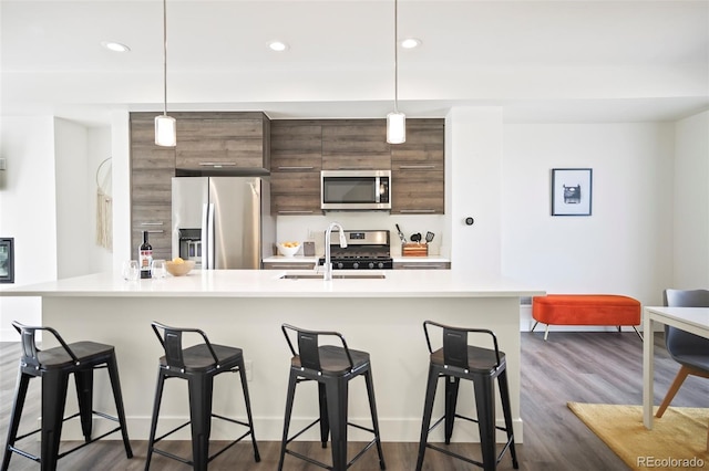 kitchen with dark wood finished floors, stainless steel appliances, light countertops, a sink, and a kitchen breakfast bar