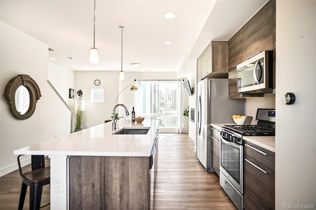 kitchen with a breakfast bar area, stainless steel appliances, a sink, light countertops, and a center island with sink