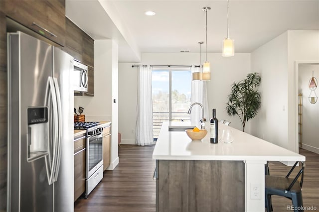 kitchen with an island with sink, dark wood-type flooring, stainless steel appliances, light countertops, and a sink