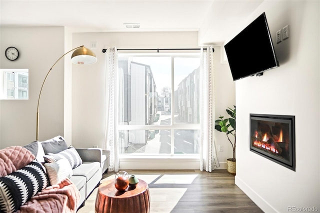 living room with a glass covered fireplace, visible vents, baseboards, and wood finished floors