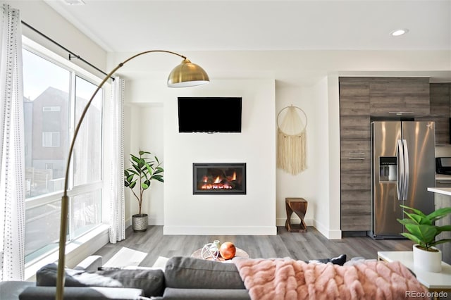 living room with a glass covered fireplace, recessed lighting, wood finished floors, and baseboards