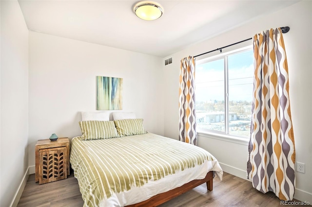 bedroom with baseboards, visible vents, and wood finished floors