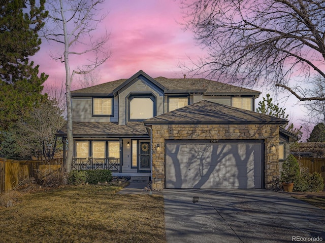 traditional home featuring fence, a porch, concrete driveway, a garage, and stone siding