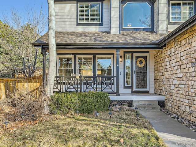 entrance to property with a porch, fence, stone siding, and roof with shingles