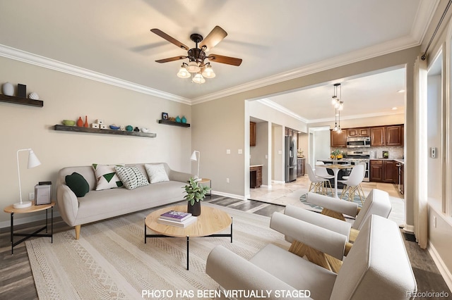 living room featuring light wood-style flooring, a ceiling fan, baseboards, and ornamental molding