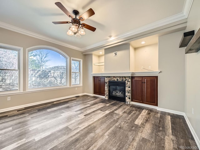 unfurnished living room with a stone fireplace, dark wood-style floors, baseboards, and ornamental molding