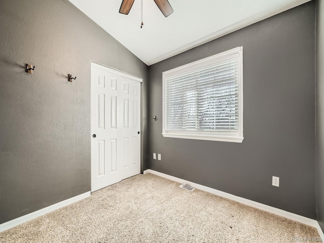 unfurnished bedroom featuring ceiling fan, baseboards, carpet floors, vaulted ceiling, and a closet