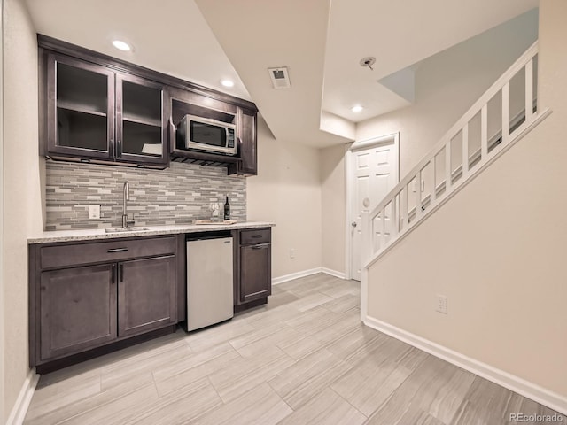 bar with tasteful backsplash, stainless steel microwave, baseboards, fridge, and a sink