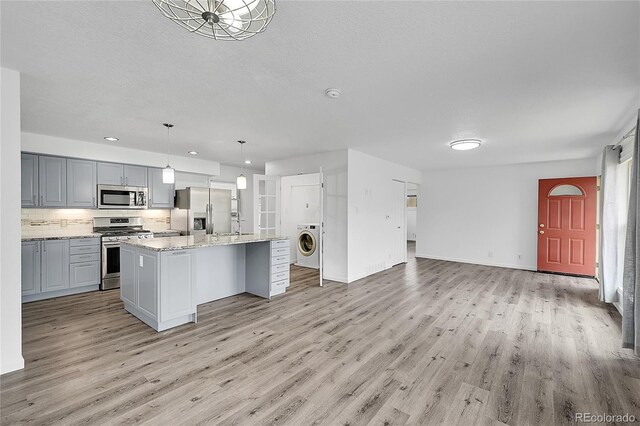 641 E 104th Pl, Northglenn, CO 80233 - kitchen with stainless steel appliances, washer / clothes dryer, light wood finished floors, open floor plan, and a textured ceiling