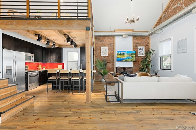 living room with a high ceiling, track lighting, a fireplace, a notable chandelier, and light hardwood / wood-style flooring