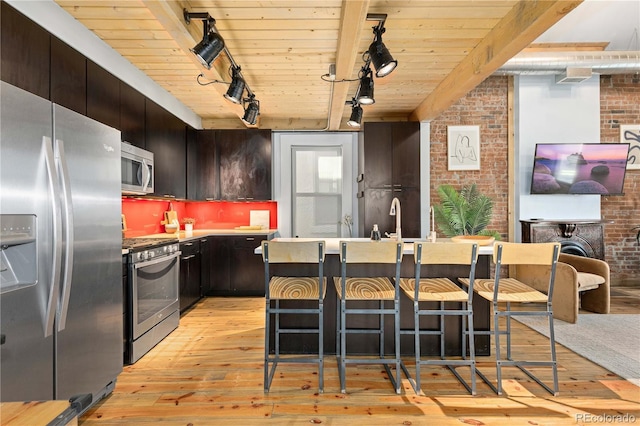 kitchen with beam ceiling, appliances with stainless steel finishes, track lighting, and wood ceiling