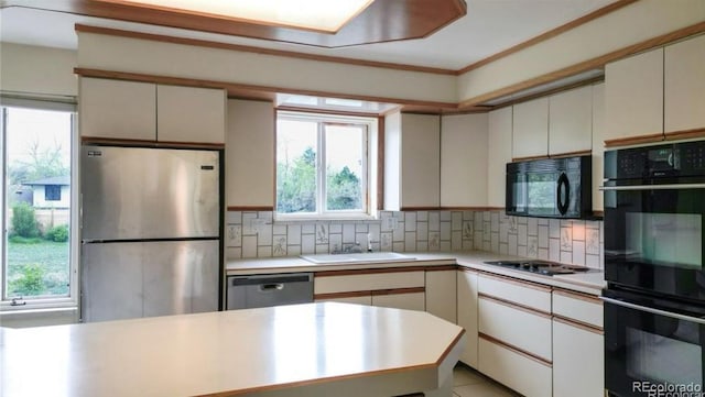 kitchen featuring a sink, black appliances, light countertops, tasteful backsplash, and a wealth of natural light