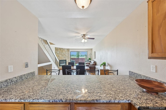 7474 E Arkansas Ave Unit 13-02, Denver, CO 80231 - kitchen with ceiling fan, a textured wall, brown cabinetry, a peninsula, and light stone counters