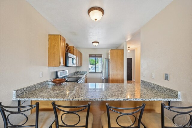 7474 E Arkansas Ave Unit 13-02, Denver, CO 80231 - kitchen with stainless steel appliances, brown cabinets, a peninsula, and a kitchen breakfast bar