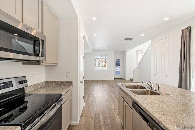 kitchen with sink, light hardwood / wood-style floors, cream cabinetry, and appliances with stainless steel finishes