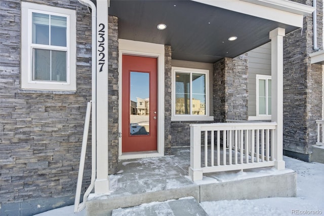 snow covered property entrance with covered porch and stone siding