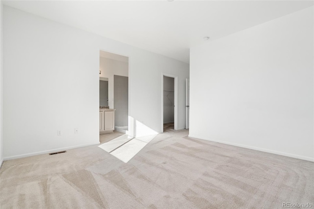 unfurnished bedroom with a walk in closet, baseboards, visible vents, and light carpet