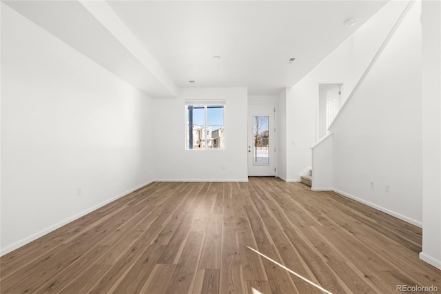 unfurnished living room with stairway, baseboards, and light wood-style floors