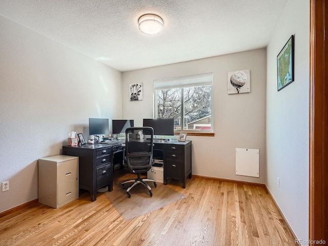 office area with a textured ceiling, light wood finished floors, and baseboards