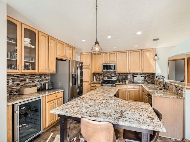 kitchen with wine cooler, decorative light fixtures, stainless steel appliances, light brown cabinetry, and a kitchen bar