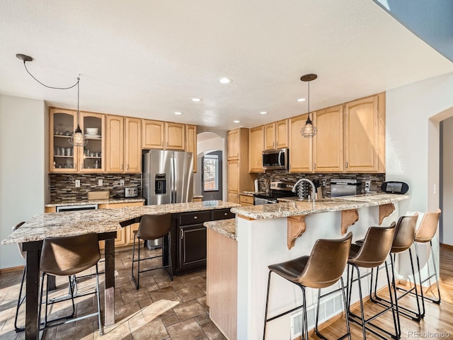 kitchen with glass insert cabinets, light stone countertops, a breakfast bar area, and stainless steel appliances