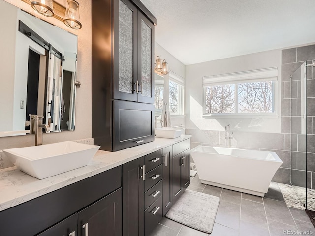 bathroom featuring tile walls, double vanity, a sink, a freestanding tub, and tile patterned floors