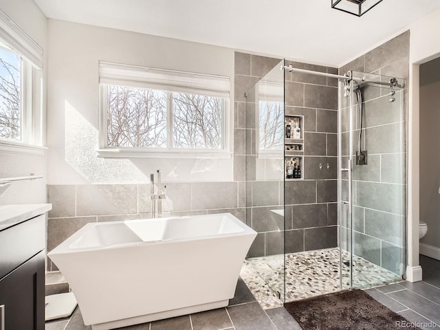 full bathroom with a soaking tub, vanity, tile walls, and tile patterned floors