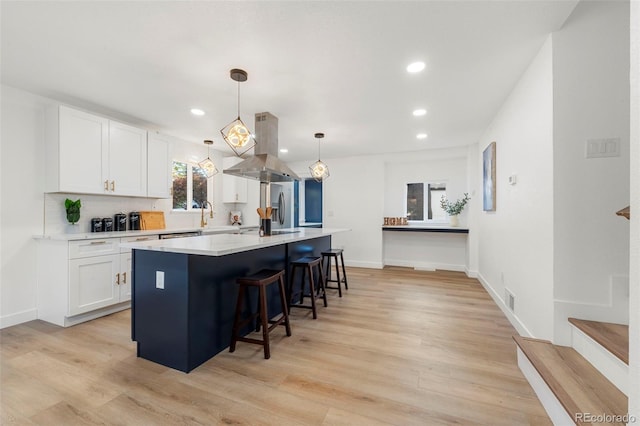 kitchen featuring island range hood, white cabinets, a kitchen island, light hardwood / wood-style flooring, and stainless steel fridge