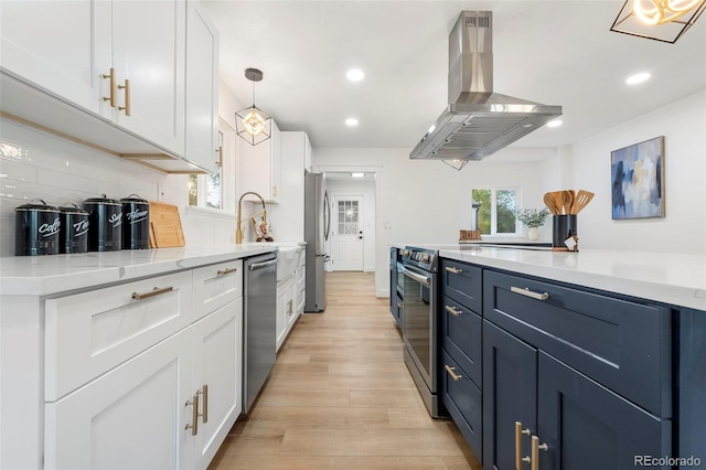 kitchen featuring island exhaust hood, appliances with stainless steel finishes, hanging light fixtures, white cabinets, and light hardwood / wood-style flooring