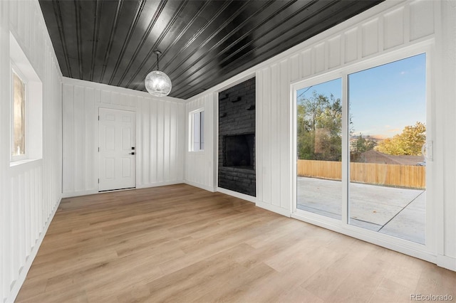 unfurnished living room with a brick fireplace, light hardwood / wood-style floors, wood ceiling, and wooden walls