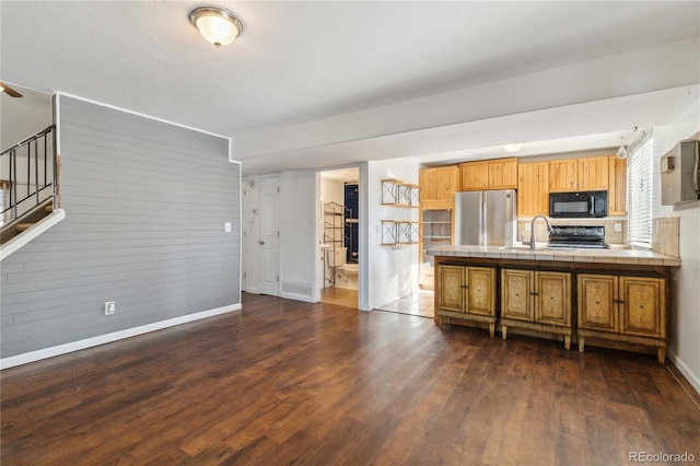 kitchen with electric range oven, tile counters, dark hardwood / wood-style flooring, wooden walls, and stainless steel fridge