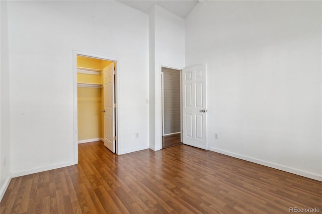 unfurnished bedroom with a high ceiling, dark wood-type flooring, a closet, and a walk in closet