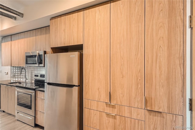 kitchen with appliances with stainless steel finishes, dark stone counters, light hardwood / wood-style flooring, sink, and decorative backsplash