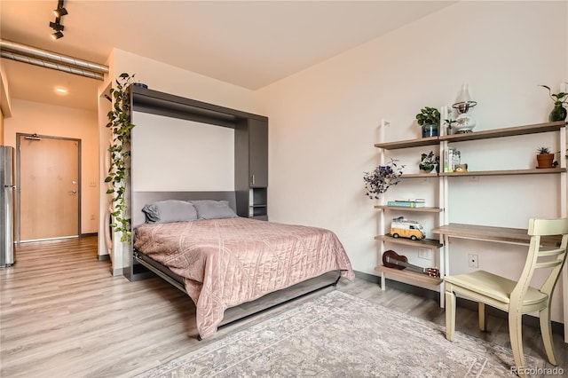 bedroom with stainless steel refrigerator, hardwood / wood-style floors, and track lighting