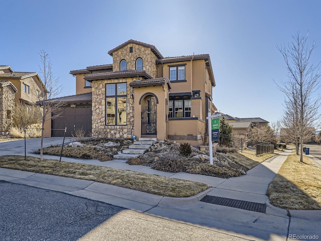 mediterranean / spanish house with stucco siding, concrete driveway, fence, a garage, and stone siding